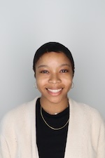 Milan Bowen smiling wearing black blouse and white sweater gray backdrop